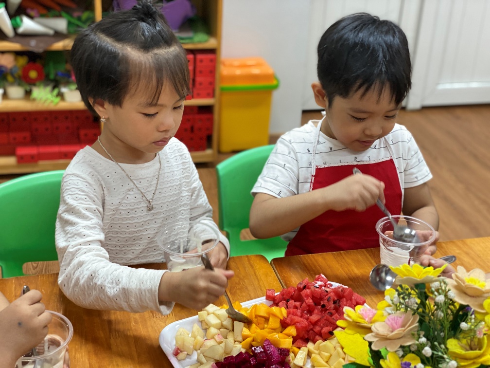 A couple of children sitting at a table eating fruit
Description automatically generated