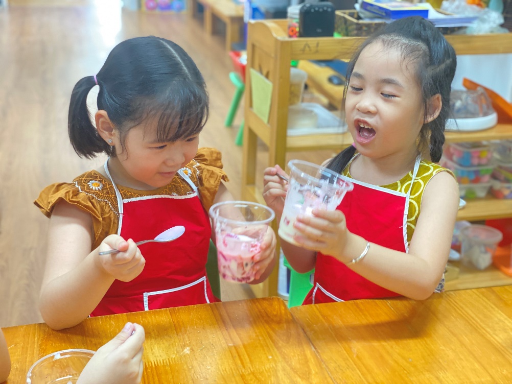 Two girls in red aprons holding cups of yogurt
Description automatically generated
