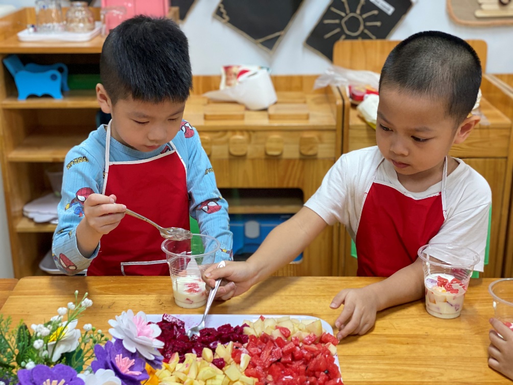 Two boys in red aprons eating fruit
Description automatically generated