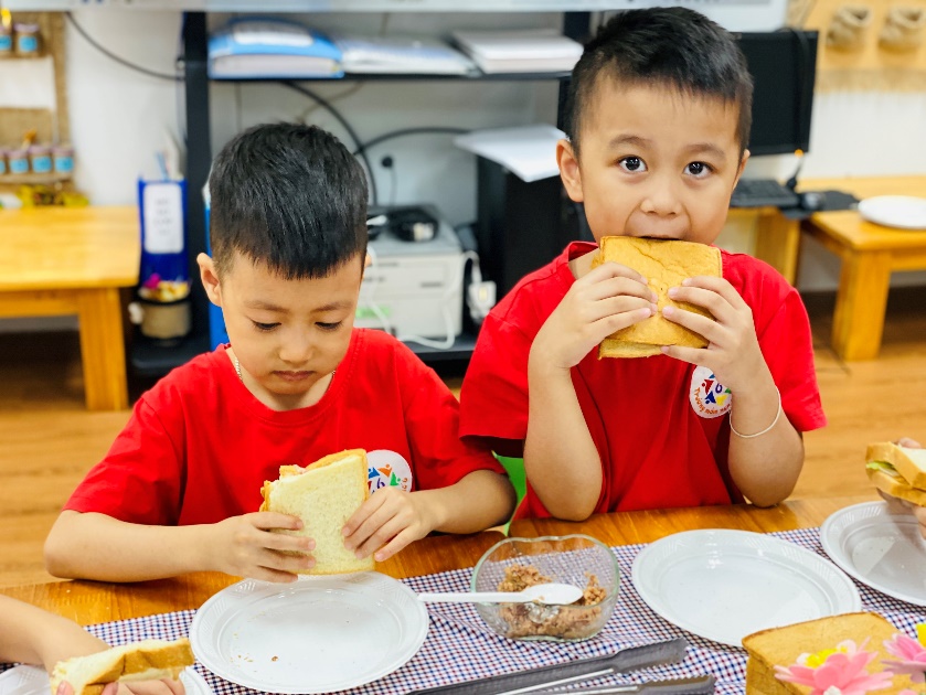 Two boys eating sandwiches at a table
Description automatically generated