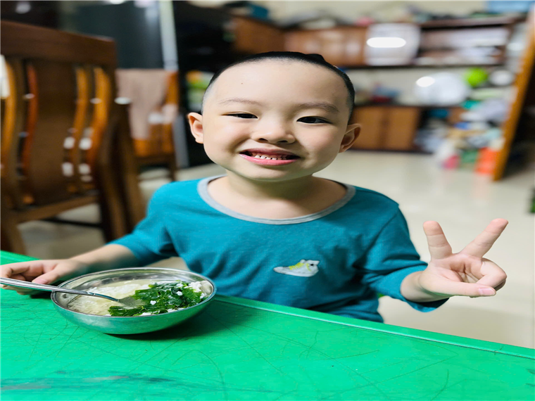 A child sitting at a table with a bowl of food
Description automatically generated