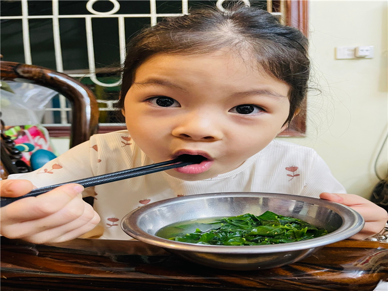 A child eating food with a spoon
Description automatically generated