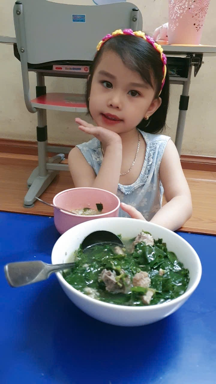 A child sitting at a table with a bowl of food
Description automatically generated