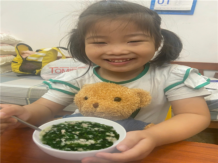 A child holding a bowl of soup and a stuffed bear

Description automatically generated