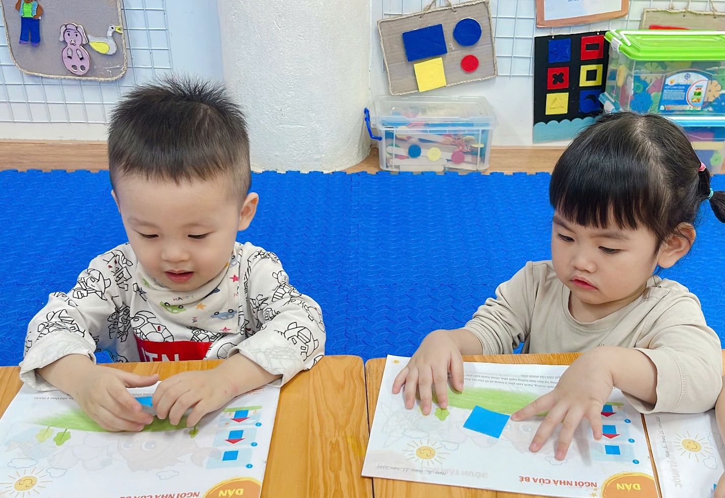 Two young children sitting at a table with paper
Description automatically generated