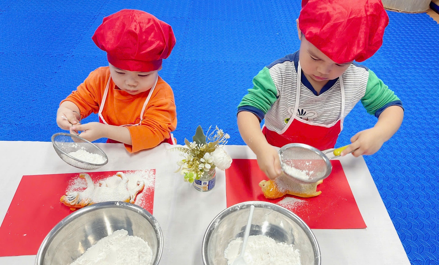 A couple of young boys in red hats making dough

Description automatically generated