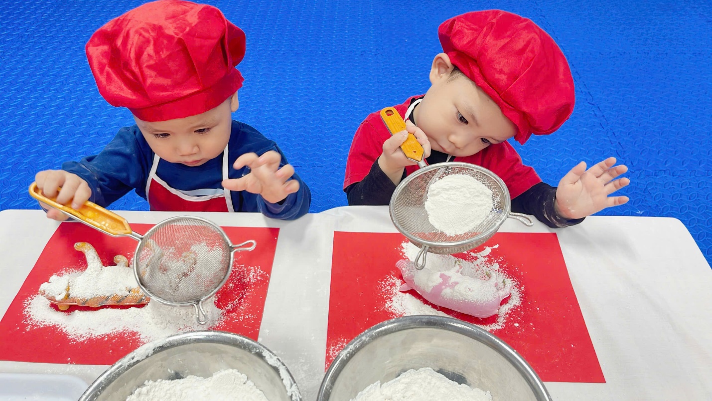 Two young boys wearing chef hats and red hats

Description automatically generated