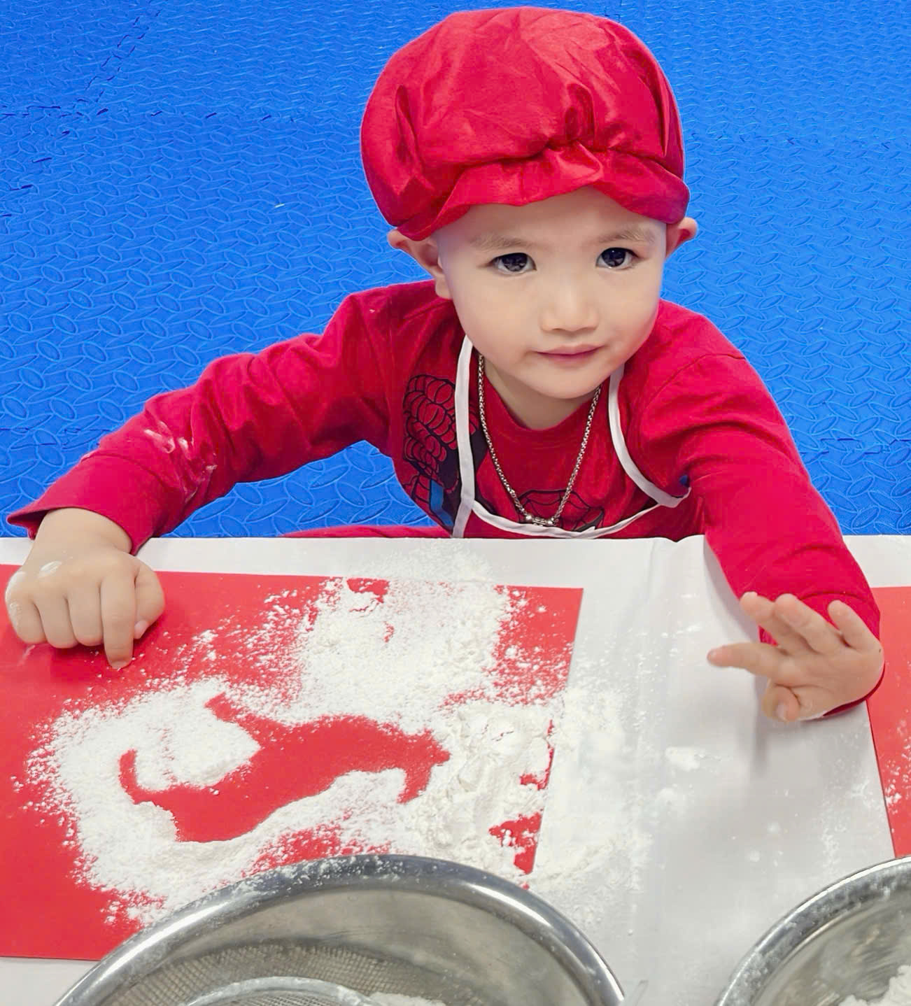 A child in a red hat and red hat with flour on a table

Description automatically generated