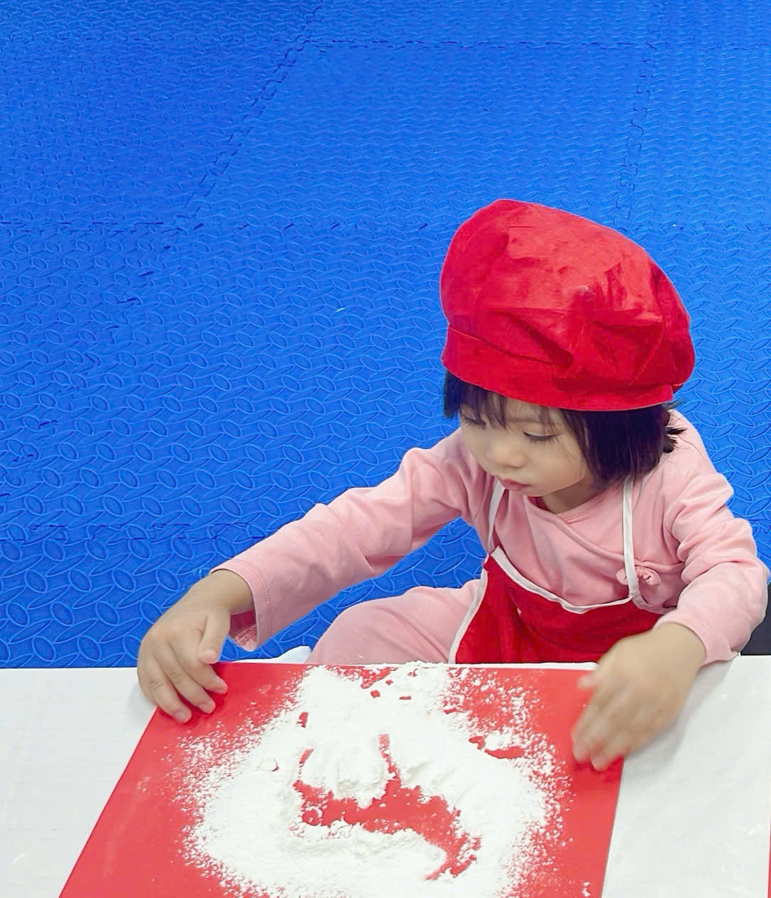 A child in a red hat and apron playing with flour

Description automatically generated