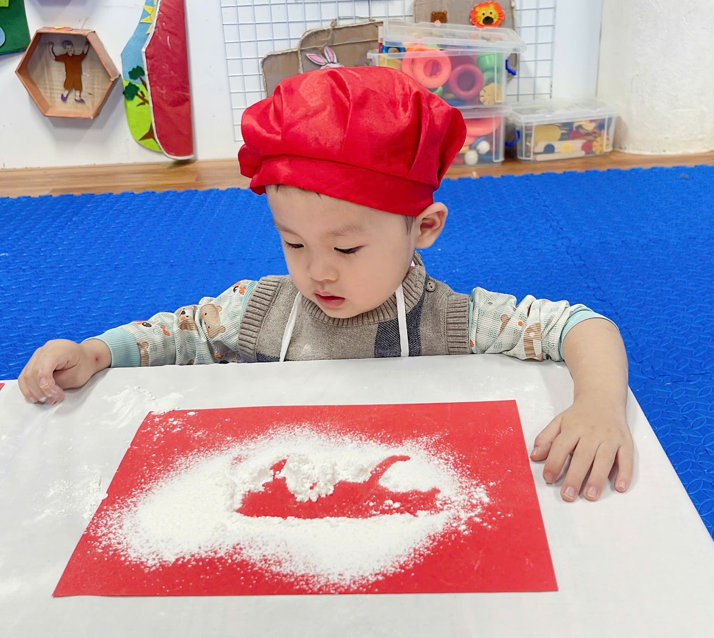 A child with red hat and white flour on a red paper

Description automatically generated