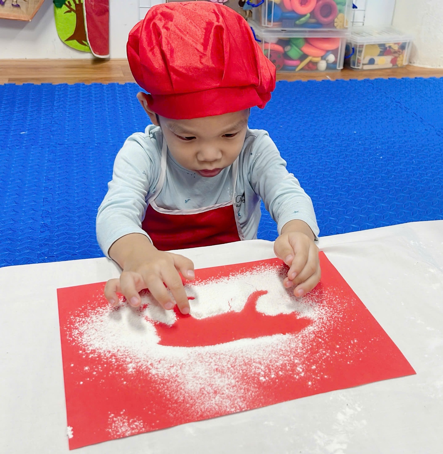 A child in a red hat and apron playing with flour

Description automatically generated