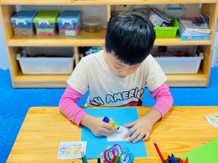 A child sitting at a table with a paper and a glue object

Description automatically generated