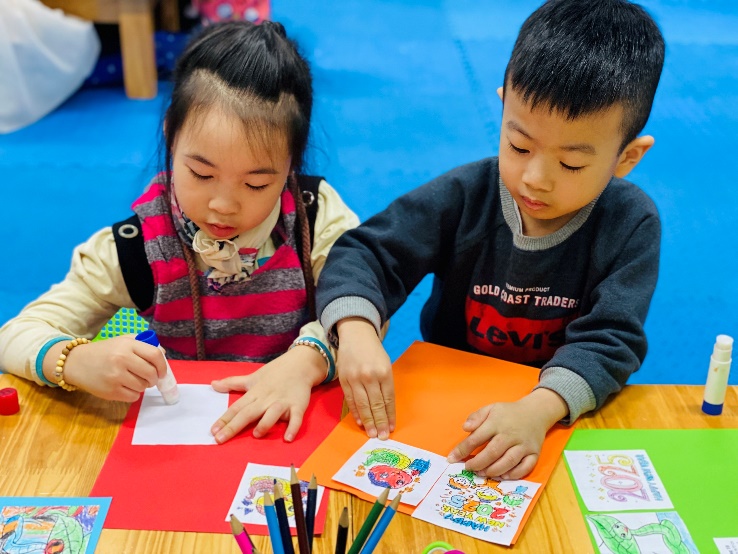 A child and child sitting at a table with colored pencils

Description automatically generated