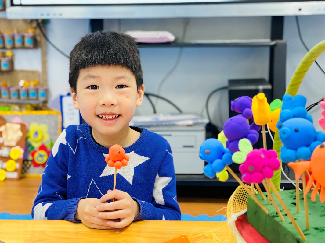 A child sitting at a table with a flower
Description automatically generated