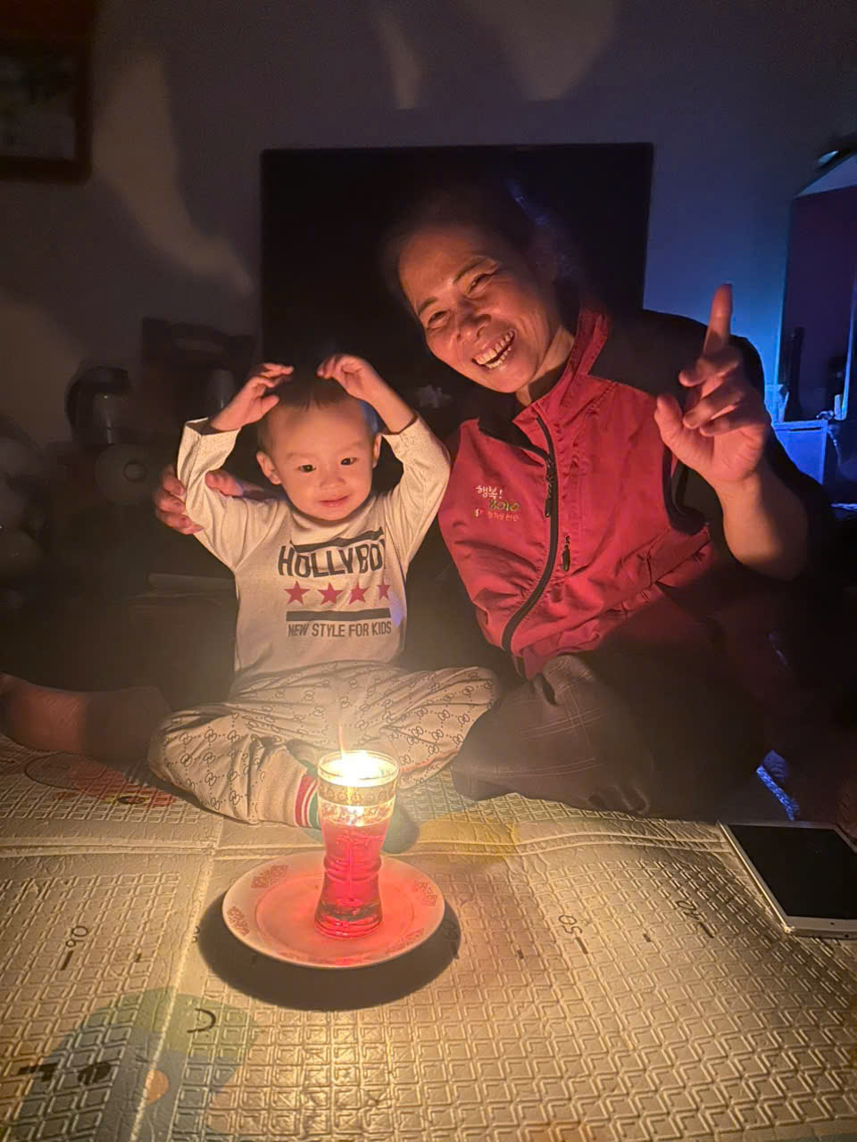 A person and a baby sitting on a table with a candle
Description automatically generated