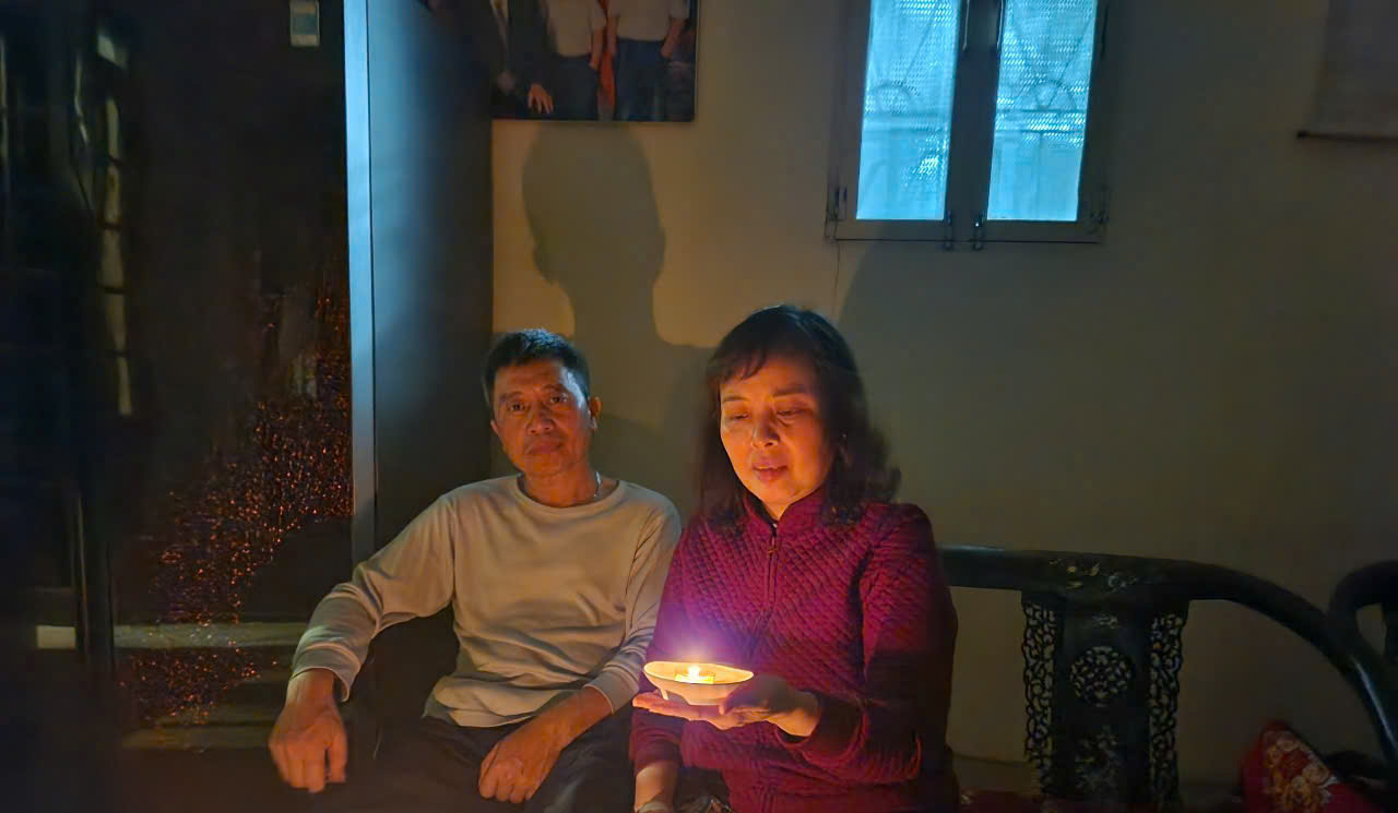 A person and person sitting in a dark room holding a candle
Description automatically generated