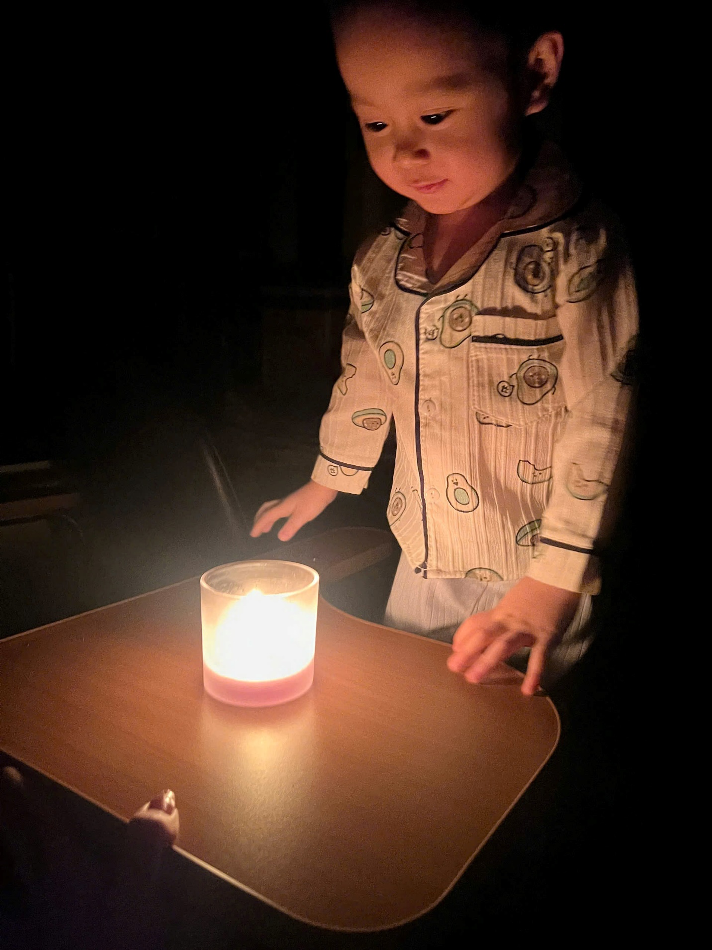 A child standing by a candle
Description automatically generated