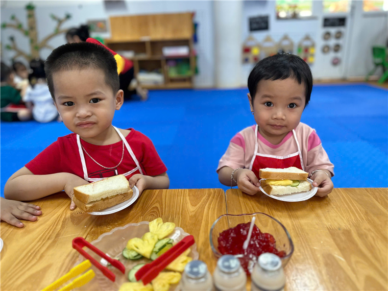 Two young boys eating sandwiches at a table
Description automatically generated